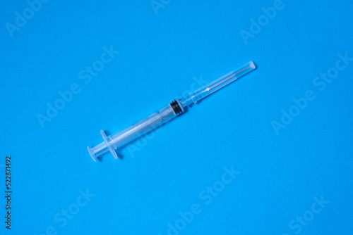 On a blue background lies a disposable plastic closed syringe, preparing for an injection, medical care