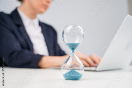 Business woman keeps track of time on an hourglass while working.