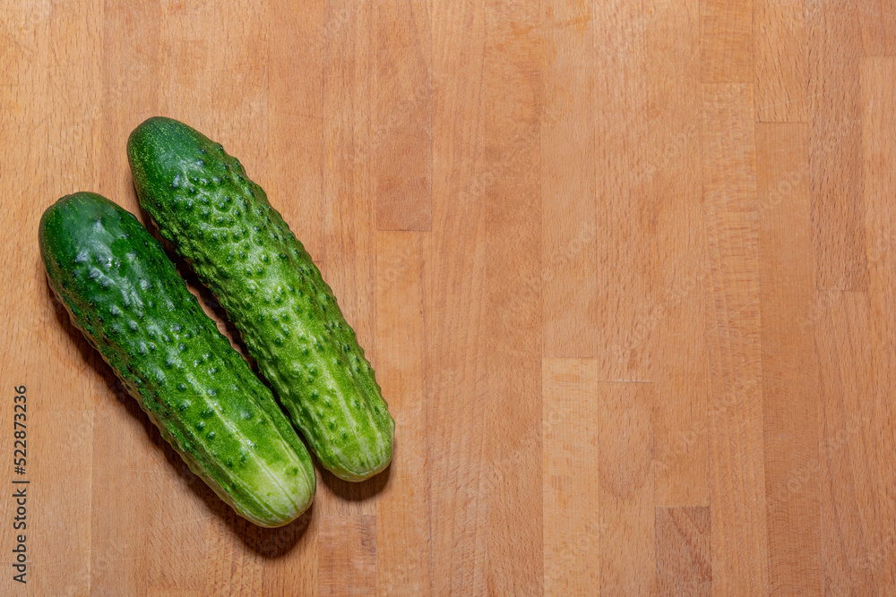 Two fresh green cucumbers lie on the left on the kitchen cutting board - the harvest is ripe, harvest, fresh green vegetables, growing vegetables, healthy lifestyle, healthy eating, cooking, ingredien Two fresh green cucumbers lie on the left on the kitchen cutting board - the harvest is ripe, harvest, fresh green vegetables, growing vegetables, healthy lifestyle, healthy eating, cooking, ingredien