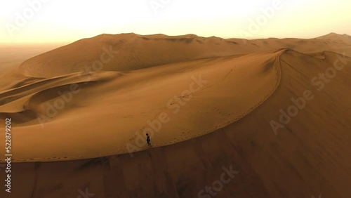 Isolated person walking and hiking on a desert sand dune alone outdoors in nature. Above view of travel guide on a big and empty hill at dawn. Adult traveling outside in a beautiful natural landscape photo