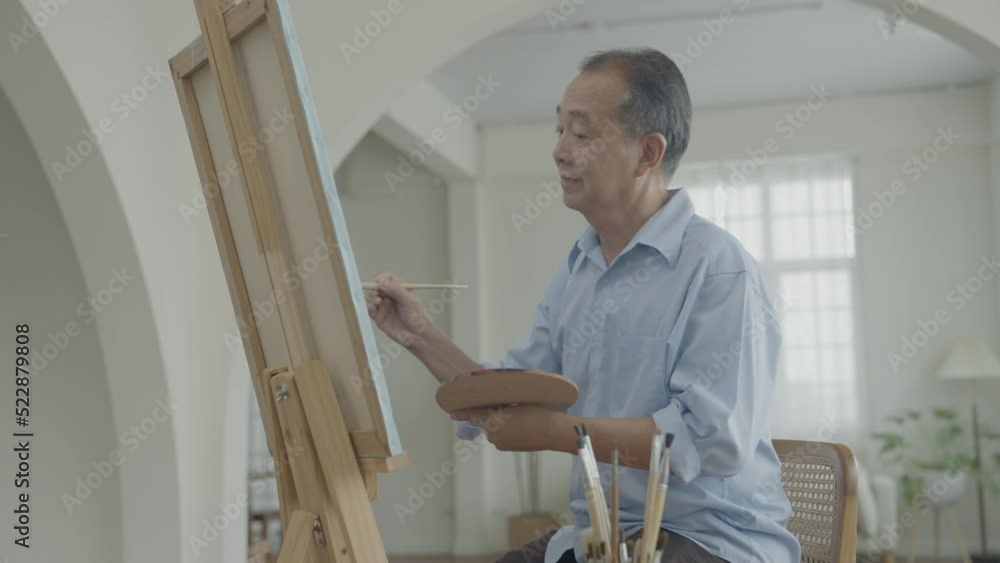 Artist concept of 4k Resolution. Asian man painting in the living room. Artist is creating work. Leisure activities and hobbies. Artist concept of 4k Resolution. Asian man painting in the living room. Artist is creating work. Leisure activities and hobbies.
