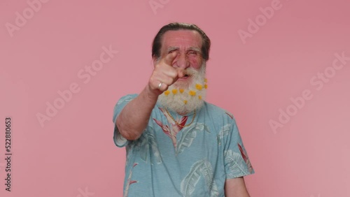 Amused senior man flowered beard pointing finger to camera, laughing out loud taunting making fun of ridiculous appearance, funny joke. Elderly grandfather posing alone on pink studio wall background