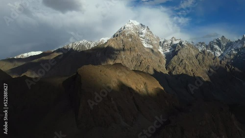 Cinematic drone shot of Tupopdan Peak, Passu Cones in Hunza Pakistan, snow covered mountain peaks with steep cliffs and shadows from clouds, rotating wide aerial shot photo