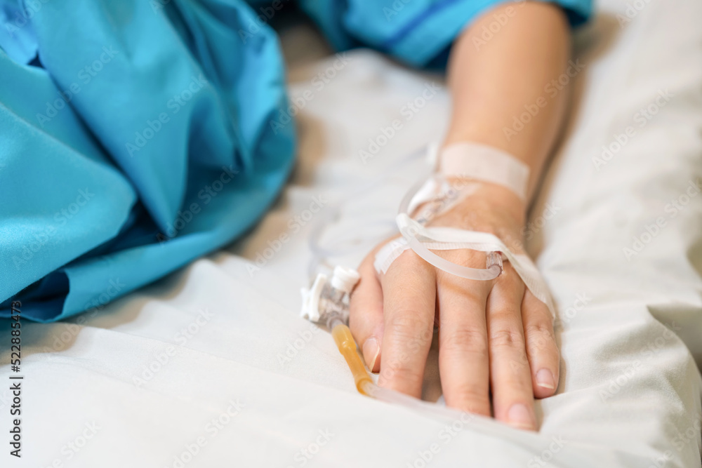 Fototapeta premium Asia patient woman lying on the bed with saline solution and syringe line on her hand in hospital ward. Emergency and treatment. Healthcare and medical concept