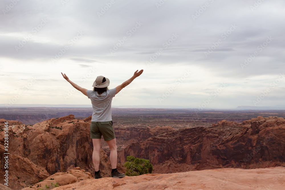 Adventurous Woman Hiking at a Desert Canyon with Red Rock Mountains. Cloudy Sky. Canyonlands National Park. Utah, United States. Adventure Travel Adventurous Woman Hiking at a Desert Canyon with Red Rock Mountains. Cloudy Sky. Canyonlands National Park. Utah, United States. Adventure Travel