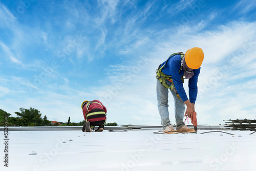 Construction worker in work clothes installing new roofing tools roofing tools, electric drill, and use on new wooden roofs with metal sheets.