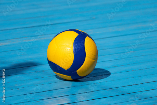 Yellow volleyball on volleyball court. The floor is made of wood and covered with blue paint. photo