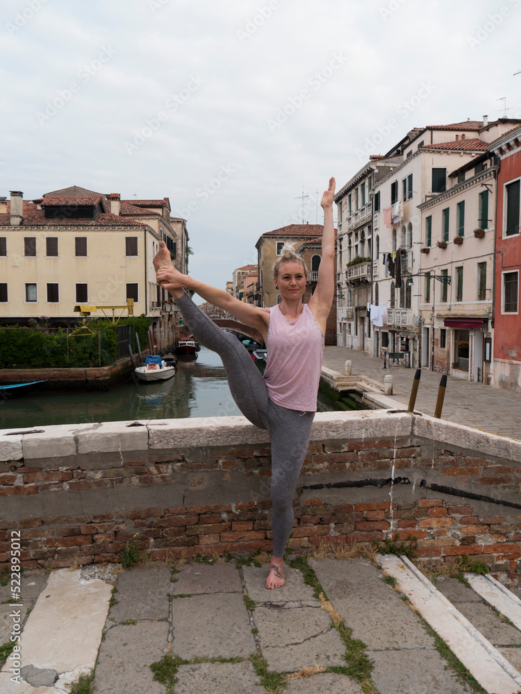 Blonde woman performing yoga poses in the city of Venice Italy.
