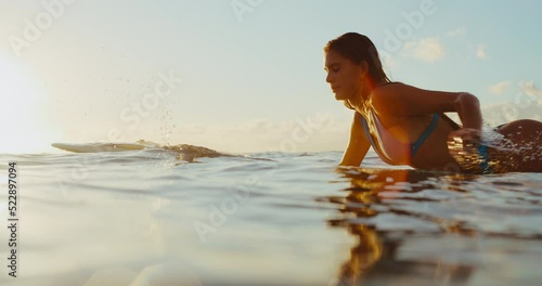 Beautiful young woman surfing at sunset, paddling out to catch the next wave, epic tropical golden hour surf session