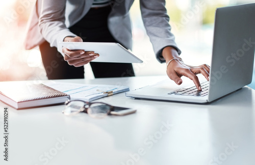 Reading, sending or checking an email or report while at work in at a professional desk. Hands typing on a laptop keyboard and holding a tablet with a business woman working in her corporate office.