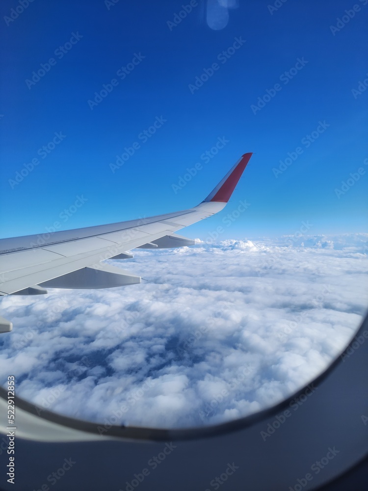 Fototapeta premium Airplane wing among the clouds and blue sky through the airplane window.