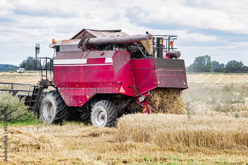 Fototapeta premium Combine in the field harvests wheat against the blue sky. Close-up.