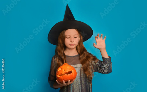 Halloween, holiday and childhood concept: european teen girl in witch costume or wizard costume holding jack-o-lantern pumpkin and showing Boo gesture.

Child looking down on a blue background.