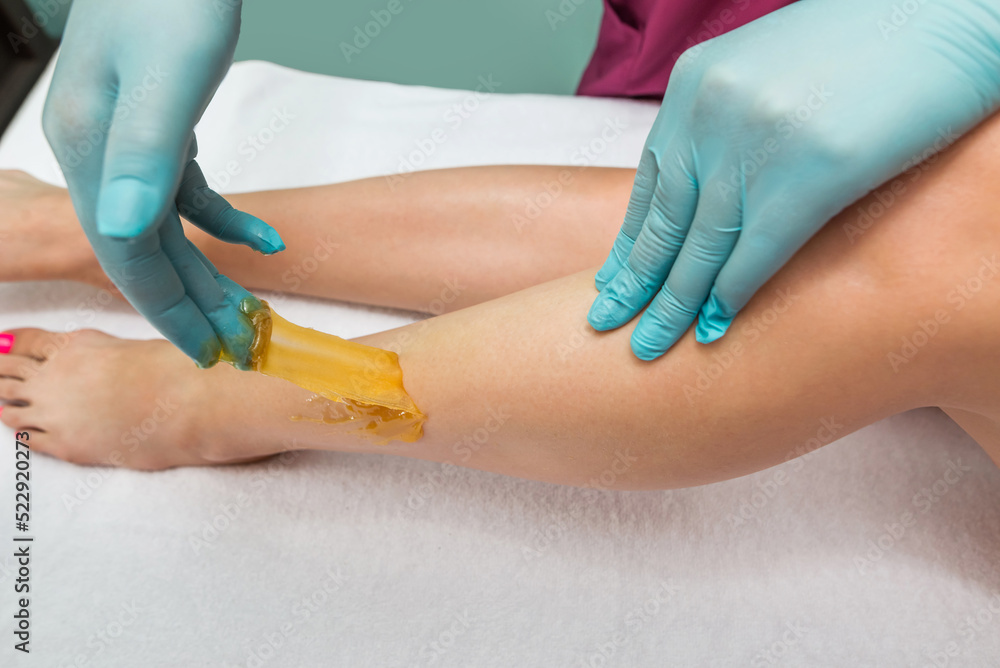 Woman undergoing leg hair removal procedure with sugaring paste in salon Woman undergoing leg hair removal procedure with sugaring paste in salon