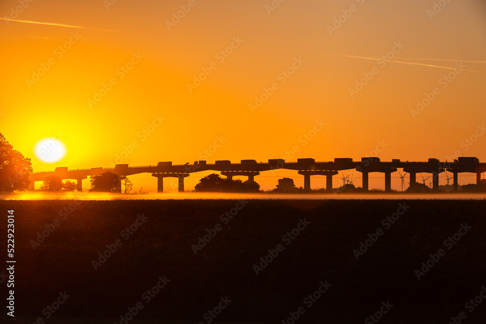 Sunrise over Ouse Bridge, M62, Goole, East Yorkshire during the heat wave in August 2022, with mist rising and wind turbines in the background.  Horizontal.  Copy space