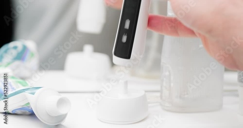 Electric toothbrush charging in bathroom. Ultrasonic toothbrush on wireless charger in bathroom. Smart black and white electric brush with colorful bristle for oral hygiene and cavity prevention.