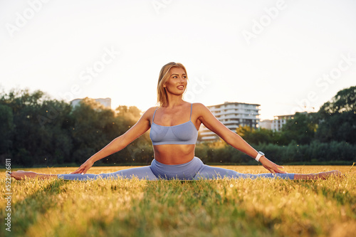 Flexible body. Beautiful woman in sportive clothes doing fitness exercises outdoors on the field