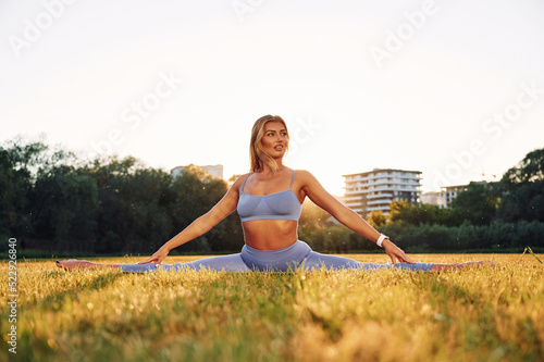 Flexible body. Beautiful woman in sportive clothes doing fitness exercises outdoors on the field