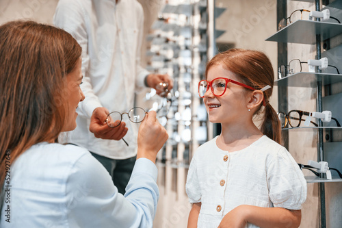 Woman, man and little girl is choosing right glasses for correcting vision