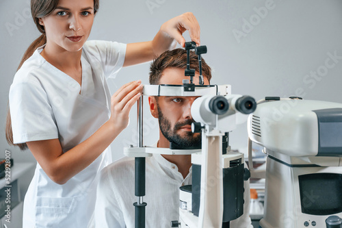 Fototapeta Naklejka Na Ścianę i Meble -  Man's vision checked by female doctor in the clinic by using special optometrist device