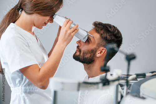 Side view. Man's vision checked by female doctor in the clinic by using special optometrist device