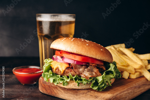 Delicious burger with beef and crispy bacon and potatoes fries on a dark background