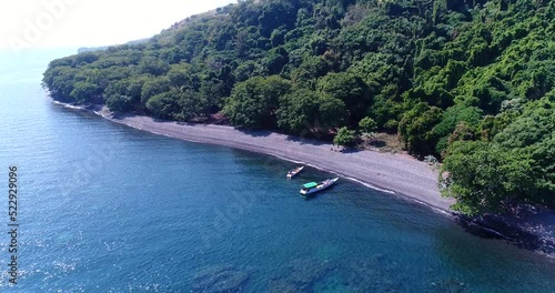 Aerial shot of small boat along tropical island with black sand beach photo