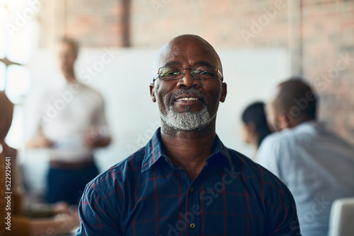 Mature business man sitting in a meeting, conference or seminar in a boardroom with colleagues at work. Closeup portrait of face of a senior, happy and corporate professional in a training workshop