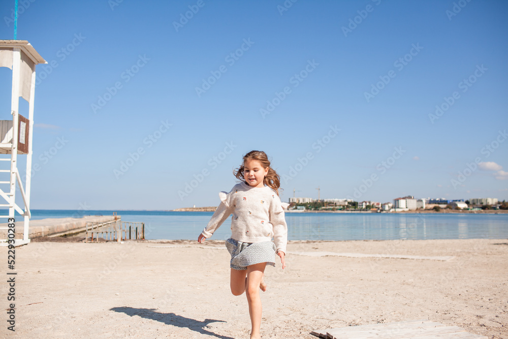 Happy female child have fun outdoor in the sand beach against the sea or ocean. Kid dress dress and sweater