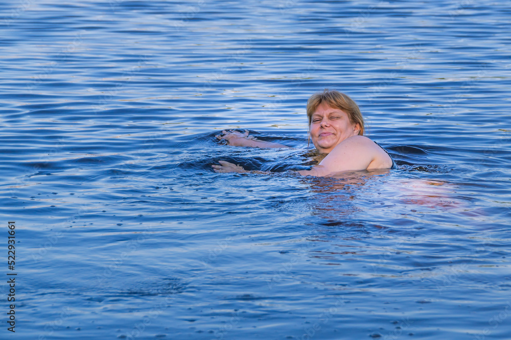 Evening swimming in the river. A woman with red hair is bathing in the river. Healthy outdoor recreation by the river. The surface of the water. Weekend in the country, in nature.