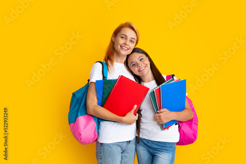 School, learning and education concept. Mother and daughter schoolgirls with school backpack and books ready to learn. Back to school. Mom and child on isolated yellow studio background. photo