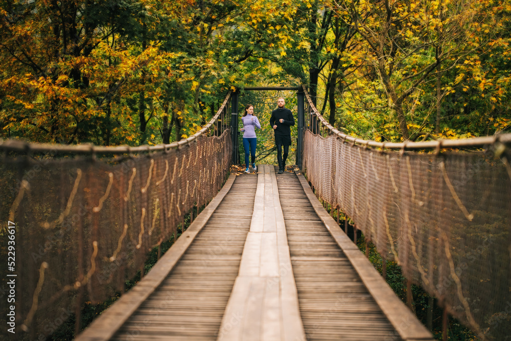 Obraz premium Young runners start jogging on a wooden suspension bridge in the middle of a mountain forest.