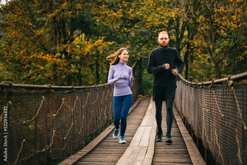 Healthy sports couple in love running together on a wooden suspension bridge.