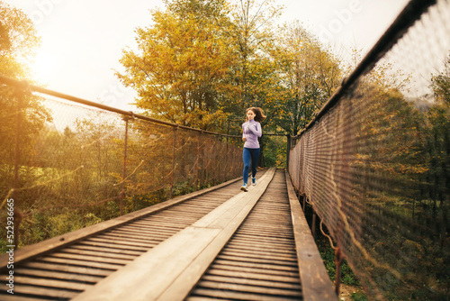 Female runner begins to jog over a wooden suspension bridge in the middle of a mountain forest.