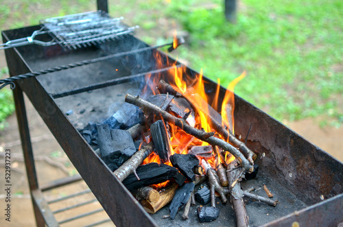 an empty brazier with a burning bonfire fire against the background of green grass preparing for a barbecue.