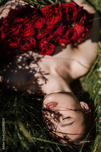 A beautiful girl poses in a field of flowers with a bouquet of red roses