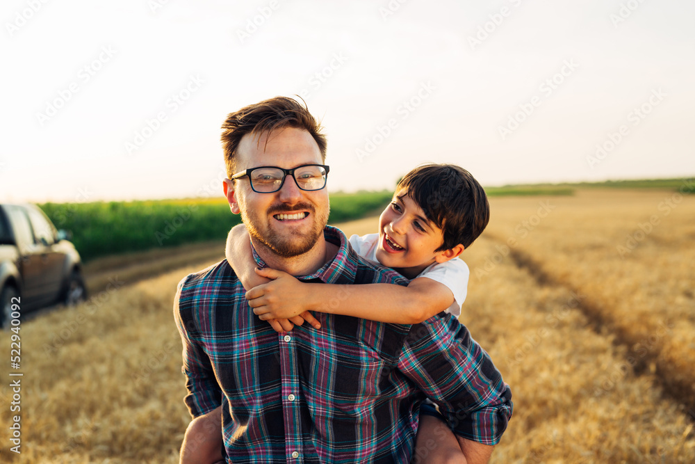 father carrying his son piggyback on wheat field father carrying his son piggyback on wheat field