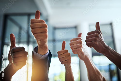 Diverse group of successful businesspeople approving and giving thumbs up for satisfaction and job well done. Corporate team of cheerful colleagues using their hands to say yes showing agreement photo