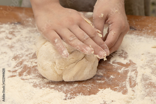 At home in the kitchen, children's hands knead a large piece of dough on a wooden table covered with flour close-up