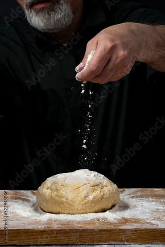 Strong male hands kneading the dough for homemade bread. Baker man kitchener in a black shirt cooking pastry
