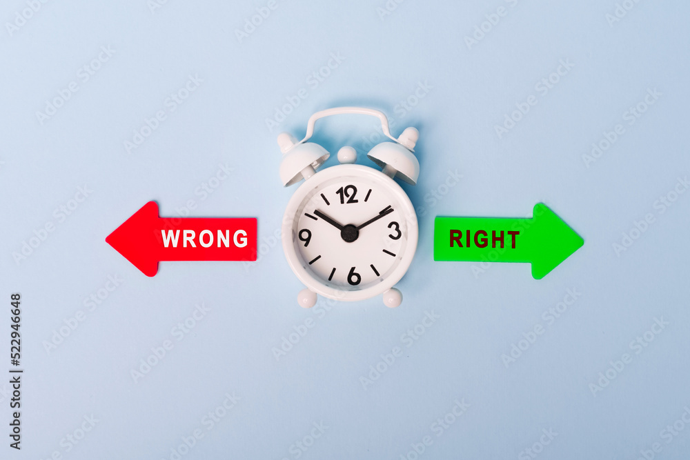 Red and green arrows with words right or wrong. Concept of choice. Two Arrows and White alarm clock on blue background, top view Red and green arrows with words right or wrong. Concept of choice. Two Arrows and White alarm clock on blue background, top view