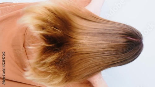 Pretty slavic girl in beige shirt demonstrates her shiny treatened long hair after therapy. Backside view. Slow motion on the white background. Closeup. Beauty, Haircare concept. photo