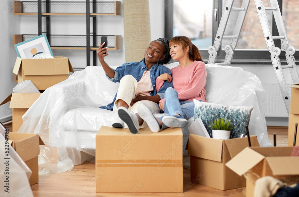 moving, people and real estate concept - happy smiling women with smartphone taking selfie at new home moving, people and real estate concept - happy smiling women with smartphone taking selfie at new home