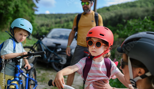 Portrait of young family with little children preapring for bike ride, standing ready with bicycles and helmet in nature. © Halfpoint