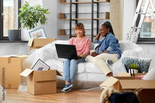 moving, people and real estate concept - happy smiling women with laptop computer and boxes at new home © Syda Productions