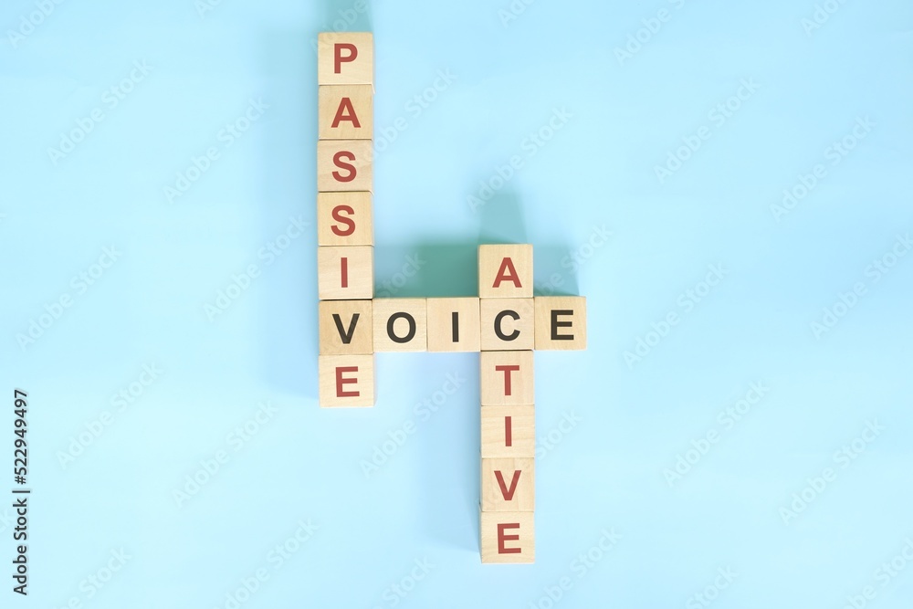 Active and passive voice topic in English grammar teaching. Wooden block crossword puzzle flat lay in blue background.