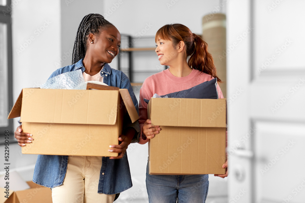 moving, people and real estate concept - happy smiling women with boxes at new home moving, people and real estate concept - happy smiling women with boxes at new home