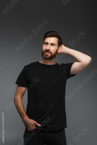 portrait of cheerful man in black t-shirt posing with hand in pocket isolated on grey.