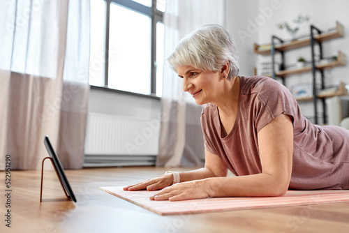 sport  fitness and healthy lifestyle concept - smiling senior woman with tablet pc computer exercising on mat at home