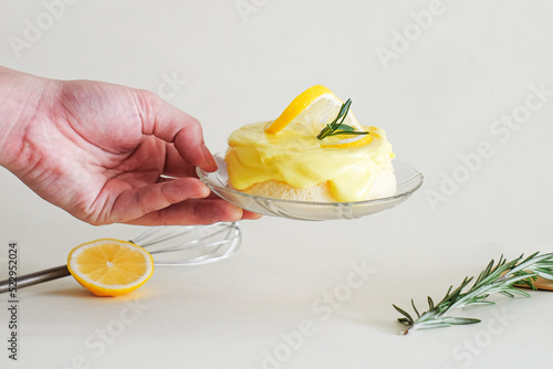 Hand hoding fresh, sweet and sour Lemon sponge or chiffon cake decorated with rosemary, lemon slice and whisk in white background and copy space. A homemade organic lemon cake for minimal cafe. photo